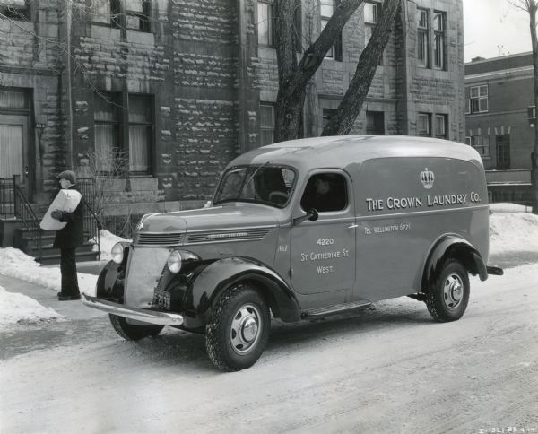 A man carries a package to a residence from an International D-15 truck owned by the Crown Laundry Company to make deliveries.