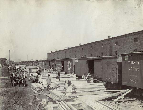 Men unload pieces of lumber from the opened boxcars of a train near the McCormick Reaper Works factory.