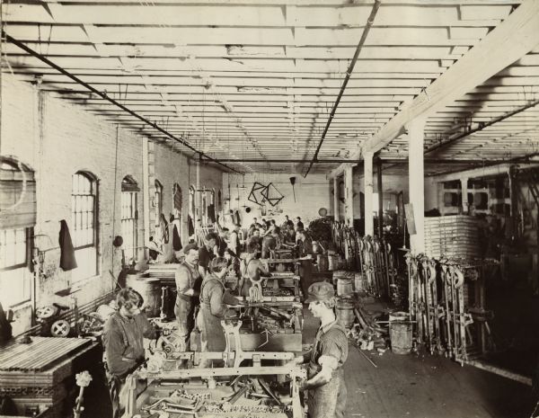 Factory workers stand at tables while working to assemble farm equipment at the McCormick Reaper Works factory.