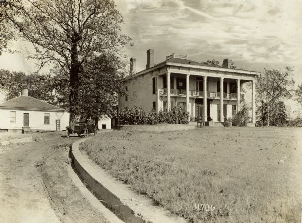 The large, pillared residence of Judge Stone, with a long driveway curving from the left. A man is driving an automobile down the driveway.