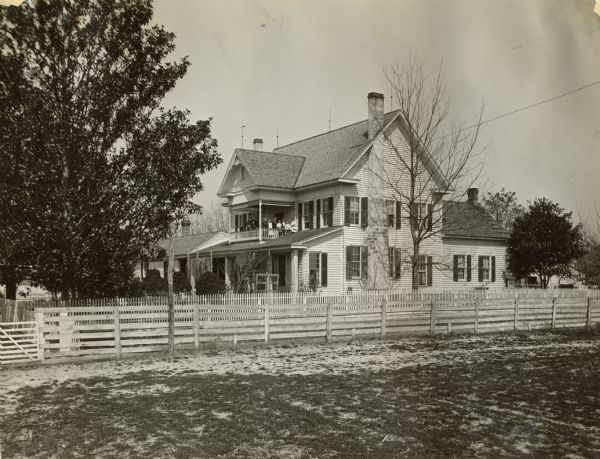 View from a field of Judge Slaughter's house. The house is surrounded by a white picket fence. On the balcony, there is a large group of people.