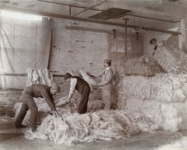 Three men open bales of sisal fiber at the McCormick Twine Mill.
