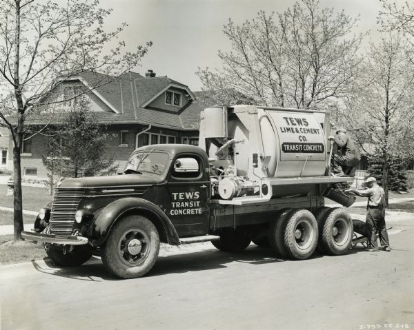 Two men standing near the back of an International D-246-F truck outfitted with a cement mixer body. The truck is owned by Tews Lime & Cement Company.