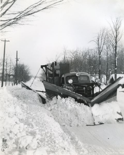 An International D-246-F truck owned by the Ontario Department of Highways clears snow from the streets of a rural area.