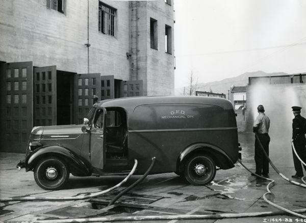 Several men use hoses running from an International Model D-2 1938 panel truck owned by the Glendale Fire Department.