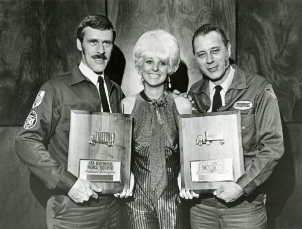 Transtar Rose (a.k.a. Bonnie Nelson) poses with ATA Roadeo winners. Original caption reads: "Transtar Rose, known to drivers across America through International Trucks late-night road condition reports, congratulates ATA Roadeo winners Richard A. Gillespie (left), who won in the Straight Truck class, and George T. Bruss, champion in the Three axle category. Gillespie drove an International CO-1610 Cargostar unit and Bruss drove a CO-1810 Cargostar tractor."