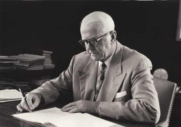 Harold B. Myers, an International Harvester Company Comptroller, looks over papers while sitting at his desk.