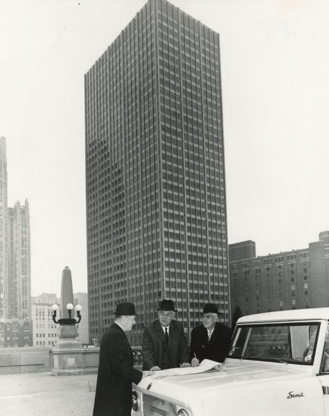 Men look over papers on the hood of an International Scout during International Harvester's move from 180 N. Michigan to 401 N. Michigan. The building in the background is 401 N. Michigan, also known as the Equitable Building.