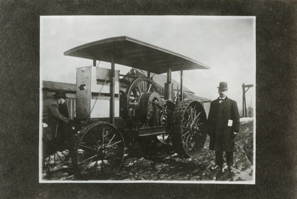 Two men standing outdoors beside a 10-horsepower tractor, possibly built by the Ohio Manufacturing Company.