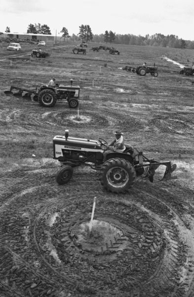 Elevated view of International Harvester employees using the company's tractors and plows to work in a field on a company farm in Tifton. International Harvester offered classes on the farm in order to provide its sales force with hands-on experience with agricultural equipment in the field.