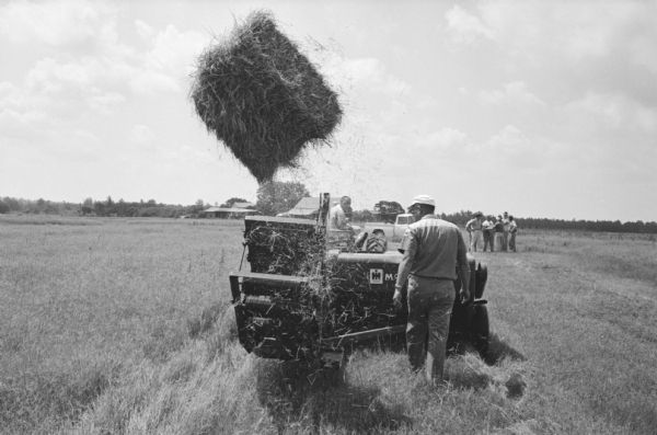 Men gather in the field on an International Harvester company farm to watch the demonstration of a bale thrower. International Harvester offered classes on the farm in order to provide its sales force with hands-on experience with agricultural equipment in the field.