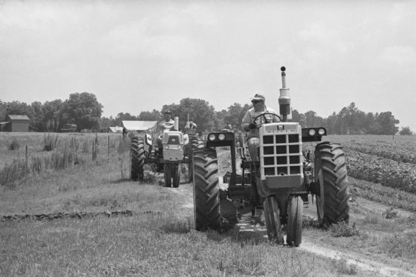 International Harvester salesmen drive tractors on a dirt road alongside a field on the company farm at Tifton. International Harvester offered classes on the farm in order to provide its sales force with hands-on experience with agricultural equipment in the field.