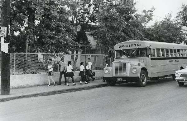 View from across street of children near a school bus in a residential neighborhood in Puerto Rico.