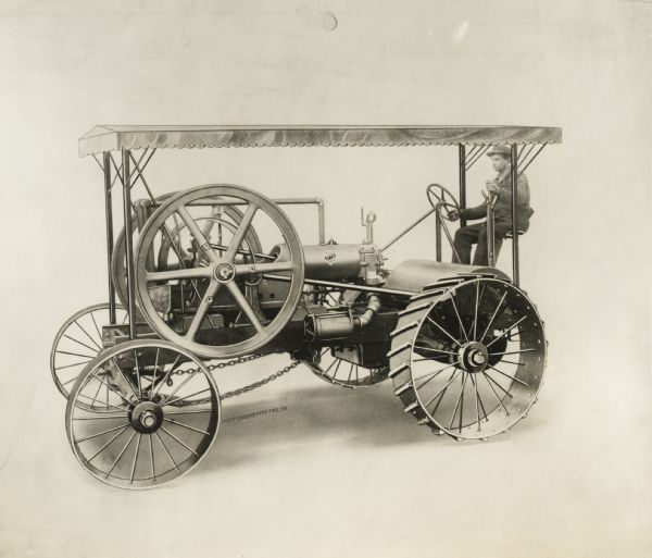 Left side view of the Otto gasoline tractor with a man behind the steering wheel.