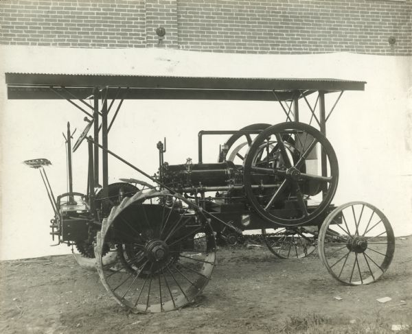 Side view of right side of an Otto gasoline engine tractor in front of a white backdrop. Behind the backdrop is the side of a brick building.