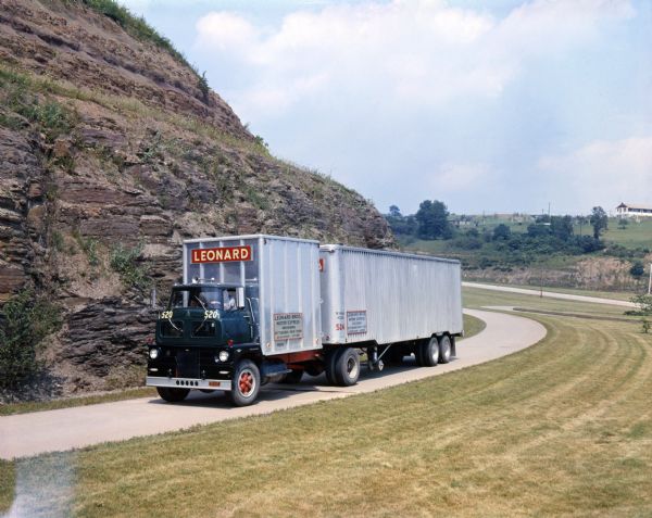 An International Sightliner ACO truck owned by the Leonard Brothers Motor Express ascends a hillside road.