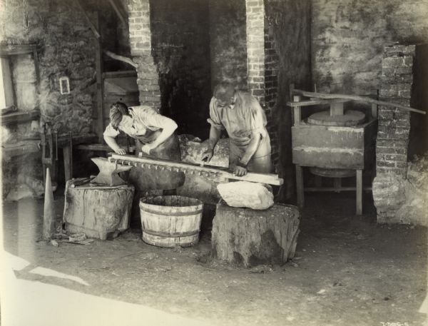 Scene from the film "Romance of the Reaper" showing the building of the first practical reaper on the McCormick farm in Virginia. Actors playing the parts of Cyrus McCormick and his slave Jo Anderson work on the reaper's cutting bar in the McCormick blacksmith shop. The film was produced to commemorate the one hundred year anniversary of the invention of the McCormick Reaper (also known as the "Reaper Centennial Celebration").