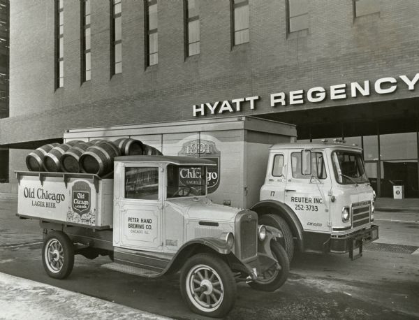 A 1927 International six-speed special and an International 1710 Cargostar-B cab-over truck parked in front of a Hyatt Regency hotel. Both trucks belonged to the Peter Hand Brewing Company. The trucks include advertising for "Old Chicago Lager Beer."