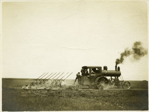 Men use an Avery 90 horsepower tractor and a gang plow to work in a farm field.