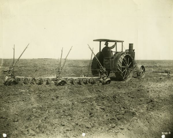 Rear view of a man using an Avery 20-35 tractor and a disc harrow to work in a field.