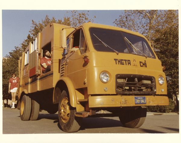 View of two members of Theta Chi fraternity with an International garbage truck. The fraternity spent a total of 3,000 hours refurbishing and converting the truck.