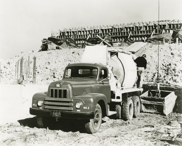 A man uses an International RF-190 series truck with a cement mixer platform body while parked in front of a partially built structure.