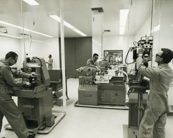 Technicians are working in a clean-room in the Solar Division of International Harvester. Original caption reads: "Much of the precise beryllium machining and fabrication for Solar's SNAP-27 project was done in this room. The hospital-clean room is air-conditioned, has glare-proof bright lights, and a built-in vacuum cleaner system and is equipped with special tools. Here, Solar's craftsmen work with metals such as beryllium, titanium, refractory metals, dispersion-strengthened metals and stainless steels and super-alloys."