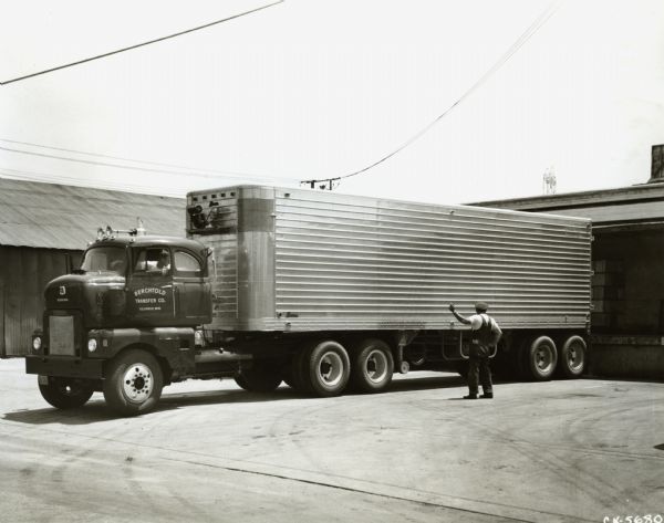 Men back an International LFCD-405 semi-truck with sleeper cab up to a loading dock. The truck was owned by Berchtold Transfer Company of Columbus, Nebraska. The press release that accompanied the original photograph reads: "COLUMBUS, NEBR. -- Four thousand miles for eggs is the round trip route run by this International LFCD-405 sleeper cab tractor owned by Berchtold Transfer company. The cab-over-engine six-wheeler, powered by a diesel engine, mounts a "sliding fifth wheel," and hauls a 35-foot aluminum body tandem axle refrigerated trailer. The unit gathers its load of 606 cases of eggs in Minnesota, Iowa and Nebraska and hauls to Los Angeles. The sliding fifth wheel permits overall length changes ranging from 45 feet, five inches to 50 feet, one inch, to meet various state length requirements. The 194-inche wheelbase tractor was built at International Harvester Company's Emeryville, Calif., plant."