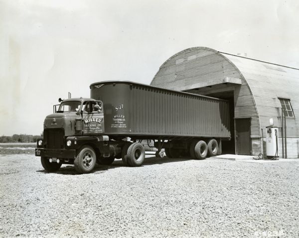 A man backing an International LCD-405 semi-truck, with sleeper cab, to a quonset-style building. The truck is owned by the Miller Trucking Company of St. Mary's, Ohio. The original press release that accompanied this photo reads (in part): "International LCD-405, Western-built diesel powered, cab-over-engine model is used by Miller Trucking Company to haul beer and rubber products from St. Mary's to Akron, Muncie and Steubenville, Ohio . . . The tandem axle semi-trailer is 32 feet long. The 116-inch wheelbase tractor was built at International Harvester Company's Emeryville, Calif., plant."
