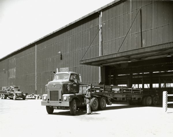 Men with an International LTCD-405 semi-truck with a load of steel bars near a Ryerson Steel Service building. The press release that accompanied the original photograph reads: "Oakland, CALIF, -- Diesel-powered International LTCD-405, a cab-over-engine model with trailing axle, operates under lease from Walkup Drayage and Warehouse Company to Ryerson Steel Service. The 134-inch wheelbase tractor, equipped with 10-speed transmission with overdrive, pulls a 35-foot, eight-inch flatbed tandem-axle semi-trailer 200 miles a day in steel-hauling service. The tractor was built at International Harvester Company's Emeryville, Calif., plant."