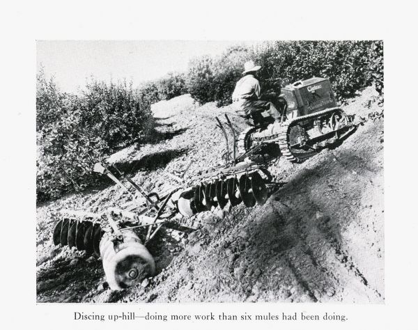 A man uses a Cletrac crawler tractor and disc harrow to do work in an uphill farm field.