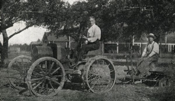 Henry Ford sitting on the 1908 model Fordson tractor. The tractor is attached to a plow, with another man sitting in the seat of the plow.