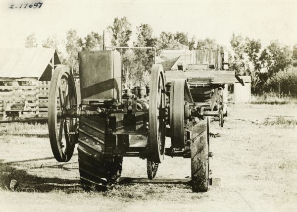 Rear view of an experimental tractor created by the Gasoline Thresher & Plow Company. Agricultural buildings are in the background.
