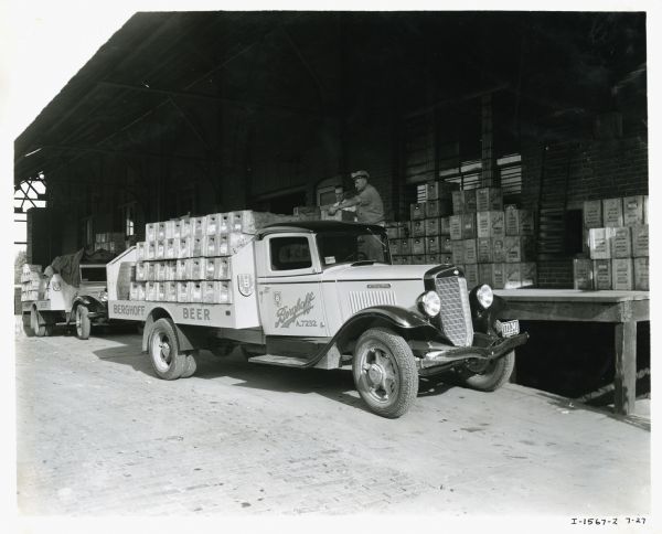 Men unload crates of beer from the back of an International C-40 truck owned by the Berghoff Brewing Company onto a loading dock.