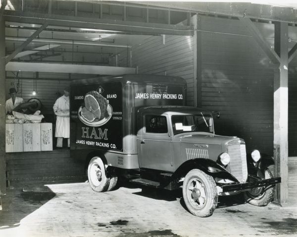 Men load meat from a loading dock onto an International C-30 truck owned by the James Henry Packing Company.