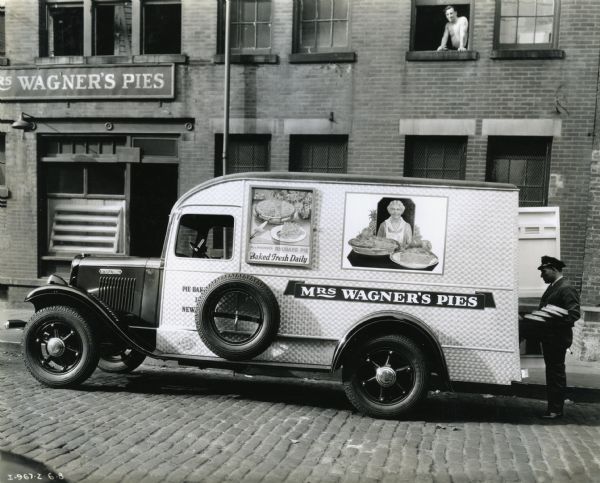 A man loads pies onto the back of an International C-line truck owned by the Pie Bakeries Company which is parked alongside a building marked: "Mrs. Wagner's Pies."