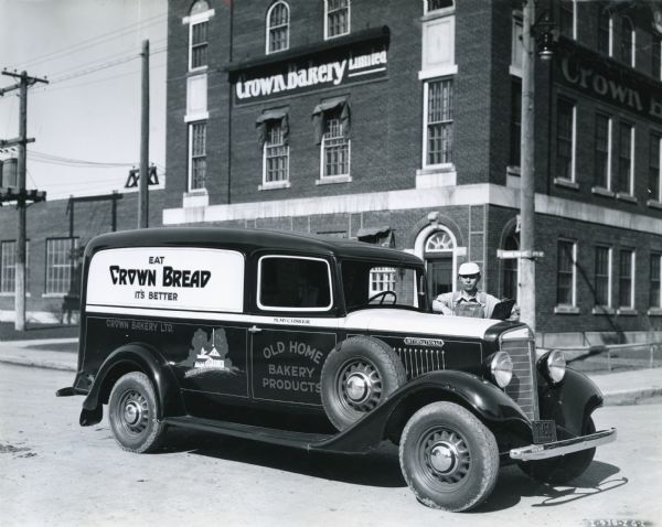 A delivery driver stands behind an International C-5 truck owned by Old Home Bakery Products. The truck is parked in front of the Crown Bakery Limited factory building.