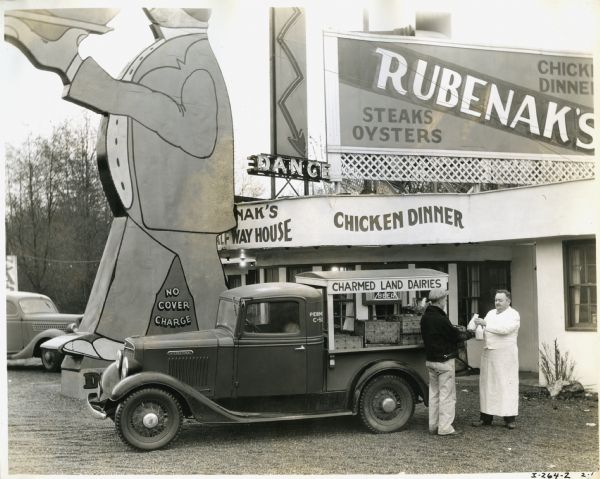 A man from Charmed Land Dairies uses an International C-1 pickup truck to deliver bottles of milk to Rubenak's, a restaurant advertised with several large signs.