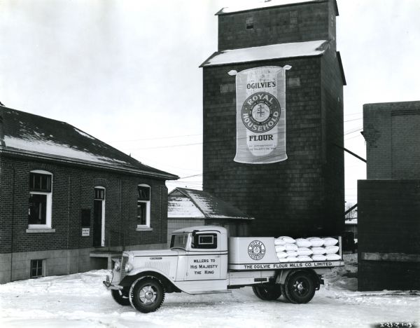 An International C-35 truck with a 175-inch wheelbase owned by Ogilvie's Flour Mills Company parked in front of the company factory. The factory was located in Edmonton, Alberta, Canada.