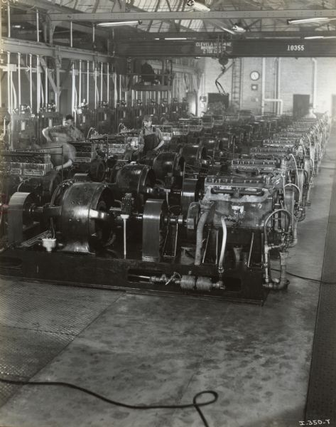 Factory workers and truck engines in the Engine Testing Room at International Harvester's Ft. Wayne Works. There is a man operating a Cleveland Crane in the background.
