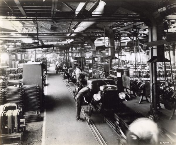 Elevated view of factory workers tending to trucks coming down an assembly line at International Harvester's Ft. Wayne Works. Stacks of truck parts are on both sides of the line.