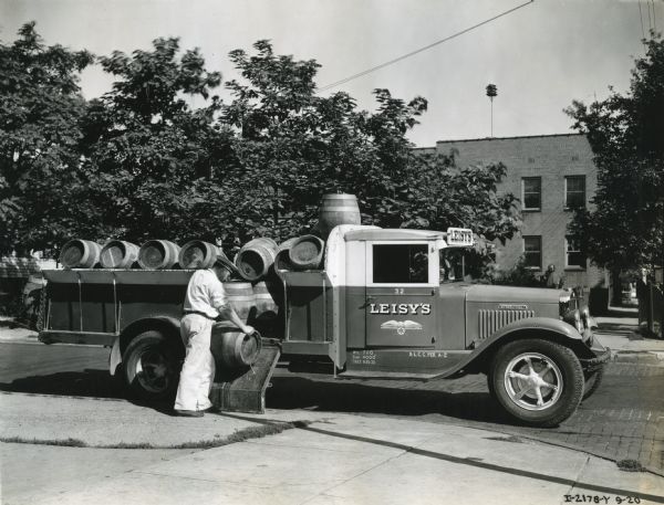 A man unloading beer barrels from the bed of an International truck owned by Leisy's Brewery.