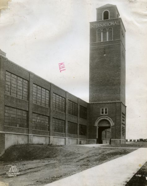 Exterior view of the newly constructed Ft. Wayne Works. The factory's distinctive north side tower is prominent. Automobiles are parked in the far background.