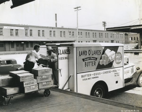 Men move wooden crates of butter from a loading dock onto the back of an International C-30 truck leased by the Land O'Lakes Company.