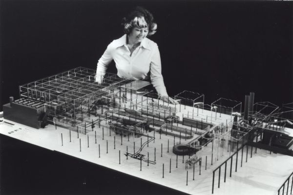 IH employee Linda Younger is standing with a scale model of a modernized foundry for the company's Louisville Works. The original caption reads: "International Harvester's Foundry Division has announced a $26.3 million modernization program at its Louisville Foundry. Heart of the program is a highly sophisticated molding system capable of producing in excess of 100 gray iron castings per hour that weigh up to 1,000 pounds. Here, Linda Younger, a Louisville Foundry purchasing department employee, views a scale model of the molding system. Construction will begin later this year and will be complete in late 1980."