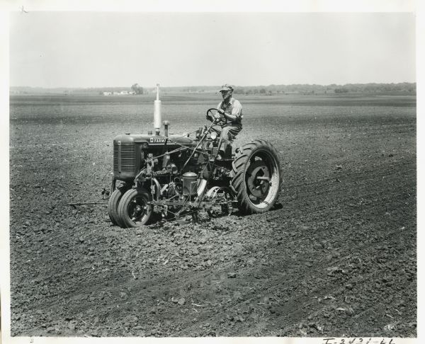Three-quarter view of a man using a Farmall C tractor in a field.