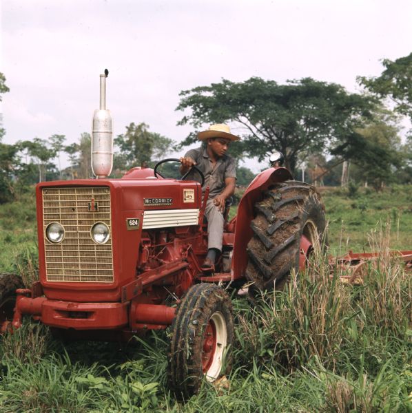 View of a man wearing a straw hat using a McCormick 624 tractor to mow a field.