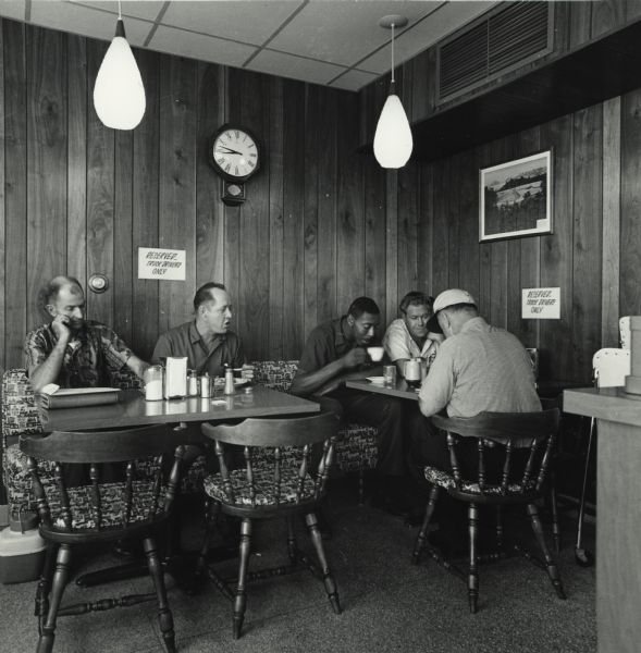 Truck drivers dining in reserved "Truck Drivers Only" seating at a diner in an American Oil Company truck stop.