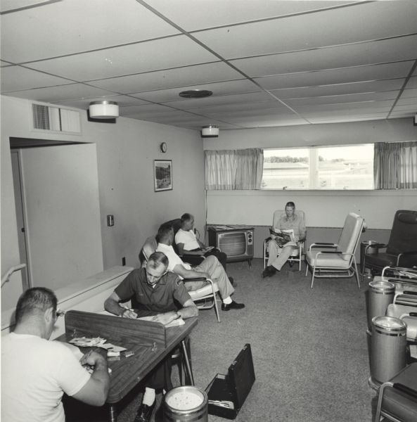 Several truck drivers relaxing in an American Oil Company truck stop lounge. Two men in the foreground are working on paperwork.