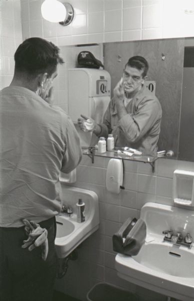 A man shaves his face in the mirror of the Mt. Victory truck stop restroom. The caption on a similar photograph reads: "Long, lonely hours on the road give way to precious minutes of conversation with fellow drivers. 'Every time I come here it's different,' Roger says. 'It's amazing the stories these fellas tell.'"